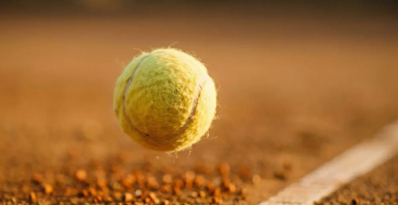 Balle de tennis en plein vol avec effet lifté visible sur court en terre battue