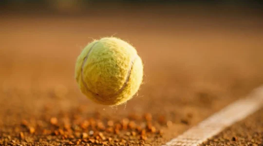 Balle de tennis en plein vol avec effet lifté visible sur court en terre battue