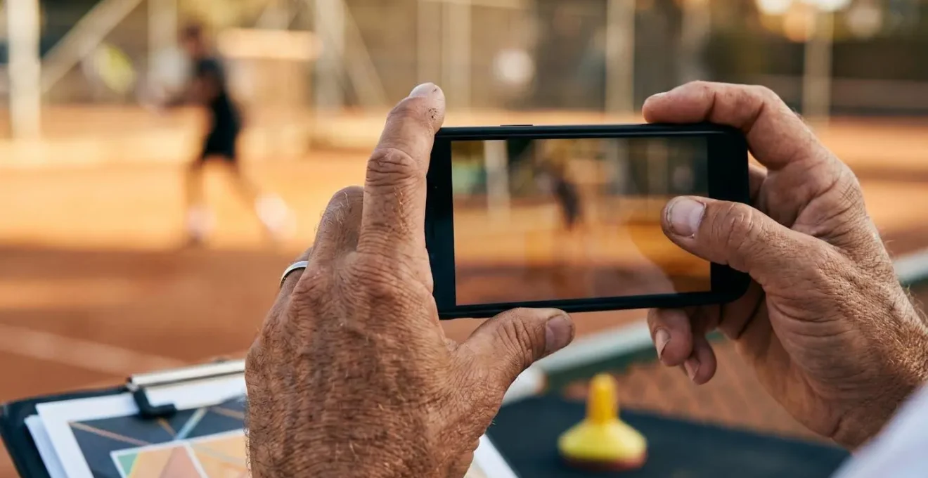 Entraîneur de tennis utilisant son smartphone pour filmer et analyser un geste technique lors d'une séance individuelle