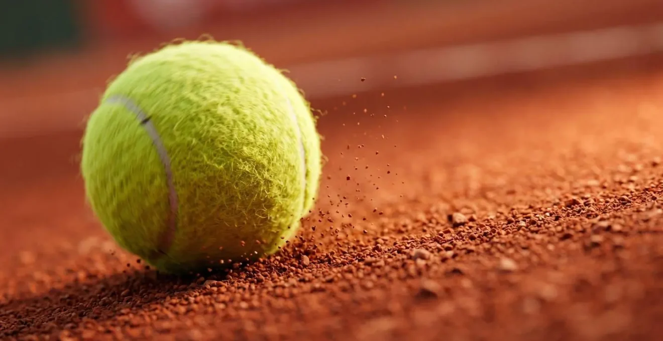Gros plan macro sur une balle de tennis en rotation captée en plein rebond sur terre battue rouge avec particules en suspension