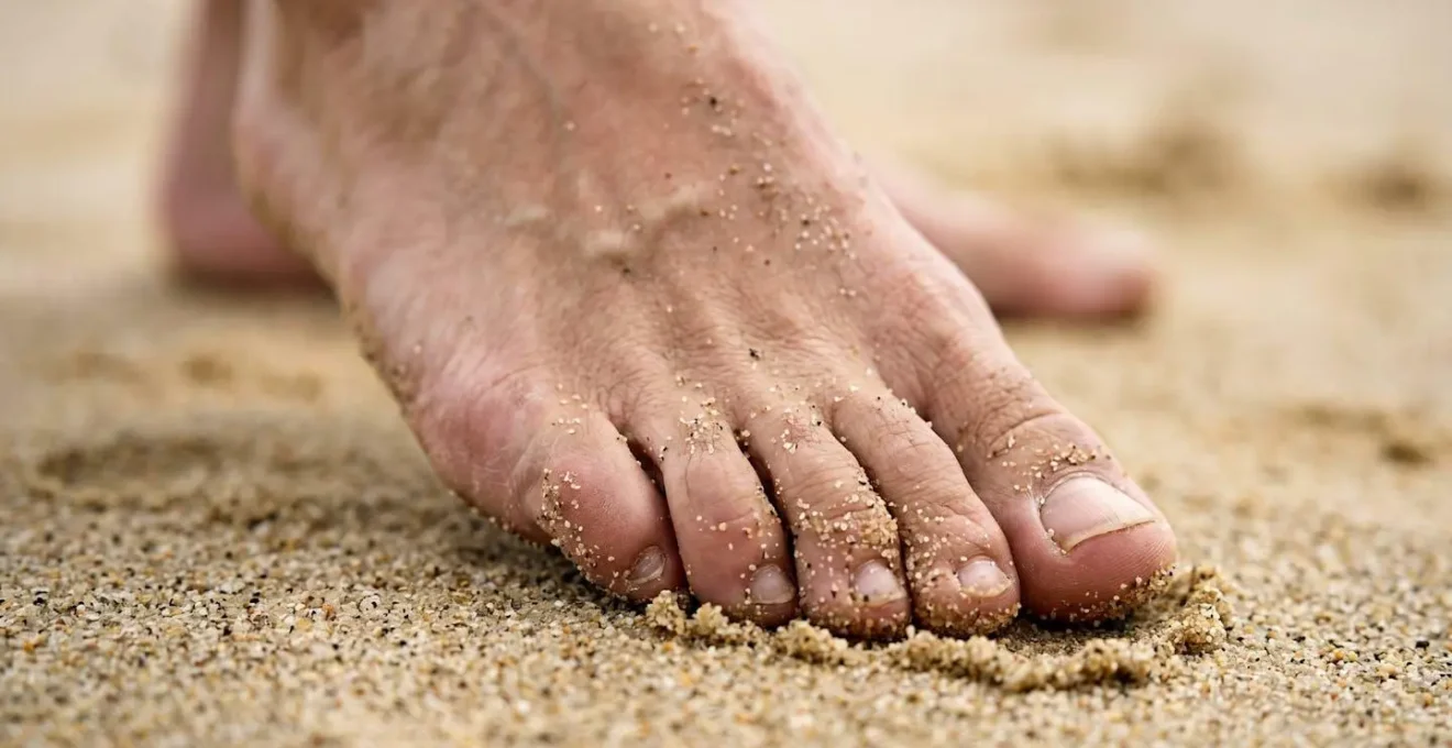 Pieds nus sur sable fin effectuant exercice d'équilibre pour renforcement chevilles et prévention blessures tennis
